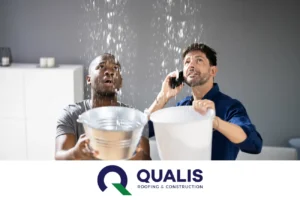 Two men collect water leaking from the ceiling using buckets. One man is on the phone, possibly arranging for immediate help to prevent further water damage. Logo at the bottom reads "QUALIS Roofing & Construction".