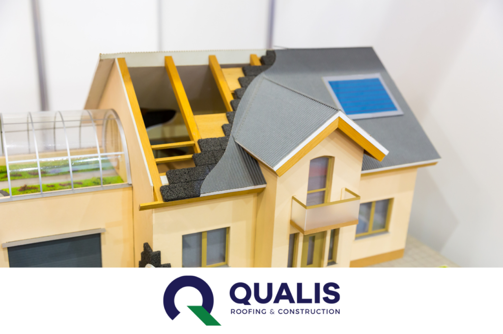 A scale model of a house with a grey roof, partially exposed beams, and a modern design, showcasing proper roof insulation. A company logo "QUALIS Roofing & Construction" is at the bottom of the image.